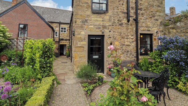 A stone building with a black door, a small window, and a garden with various plants and flowers.