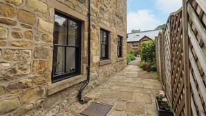 A stone building with a narrow stone pathway, wooden fence, and potted plants.