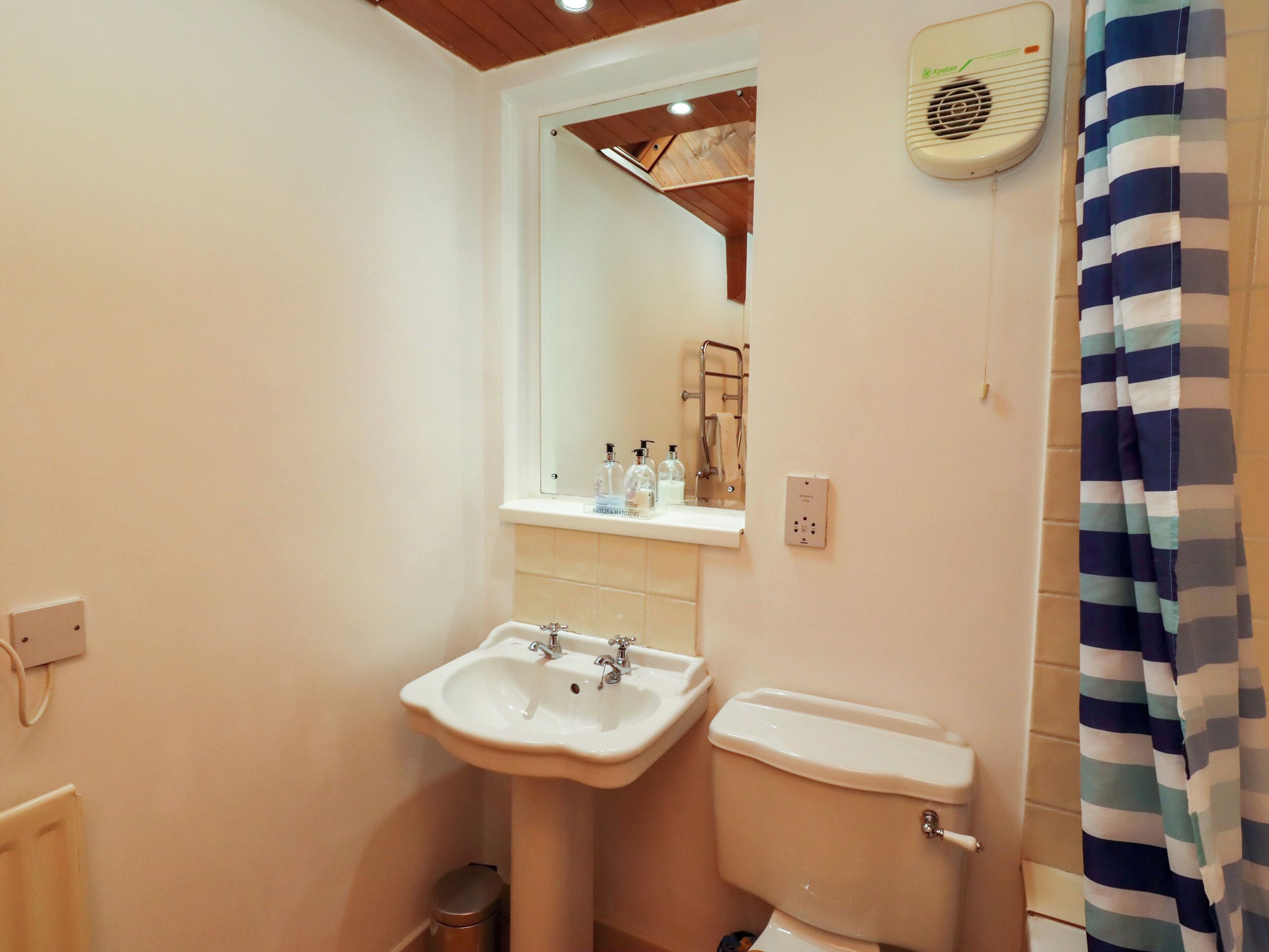 Een badkamer met wastafel, toilet, spiegel en douchegordijn.