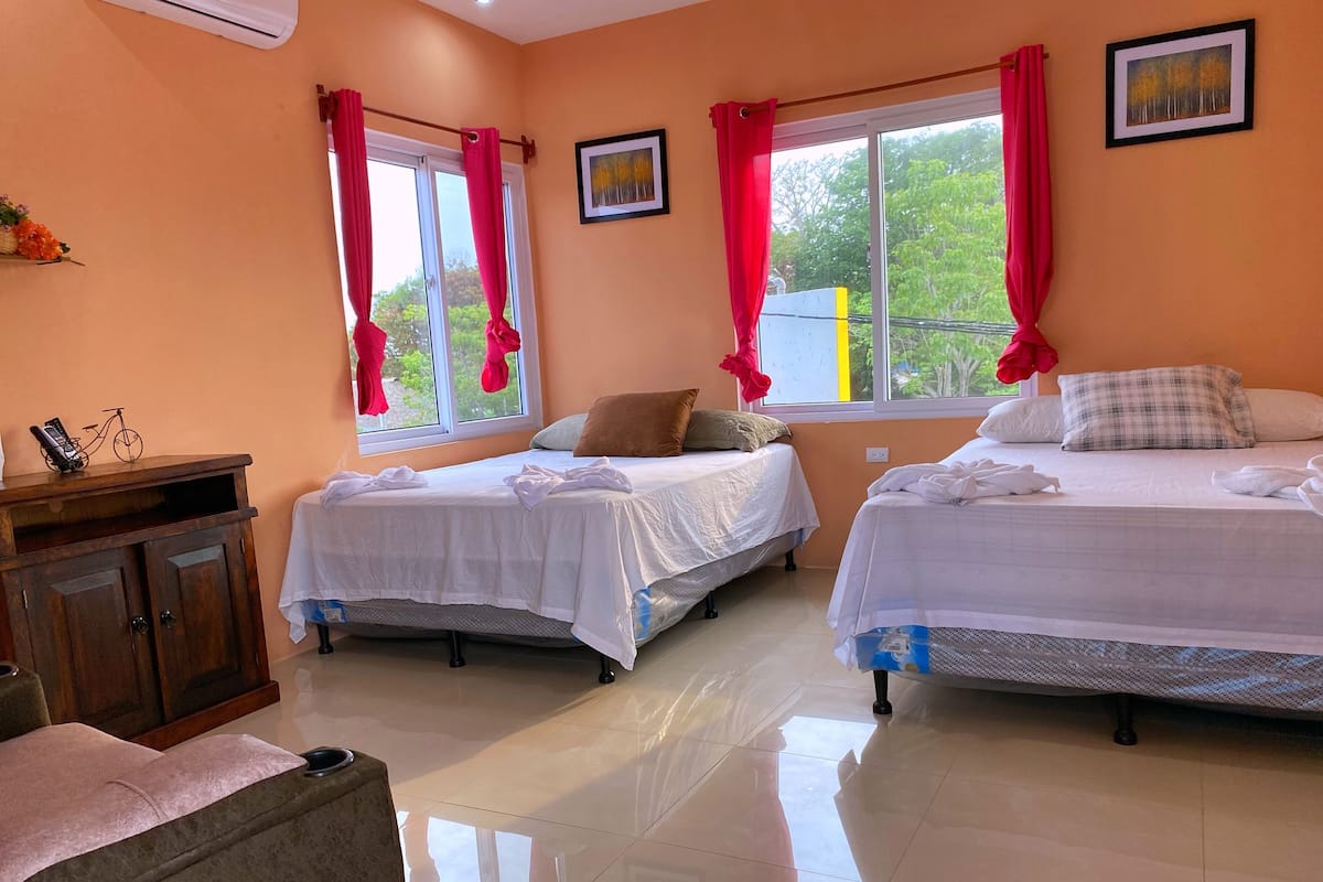 A hotel room with two beds, a wooden cabinet, and a window with red curtains.