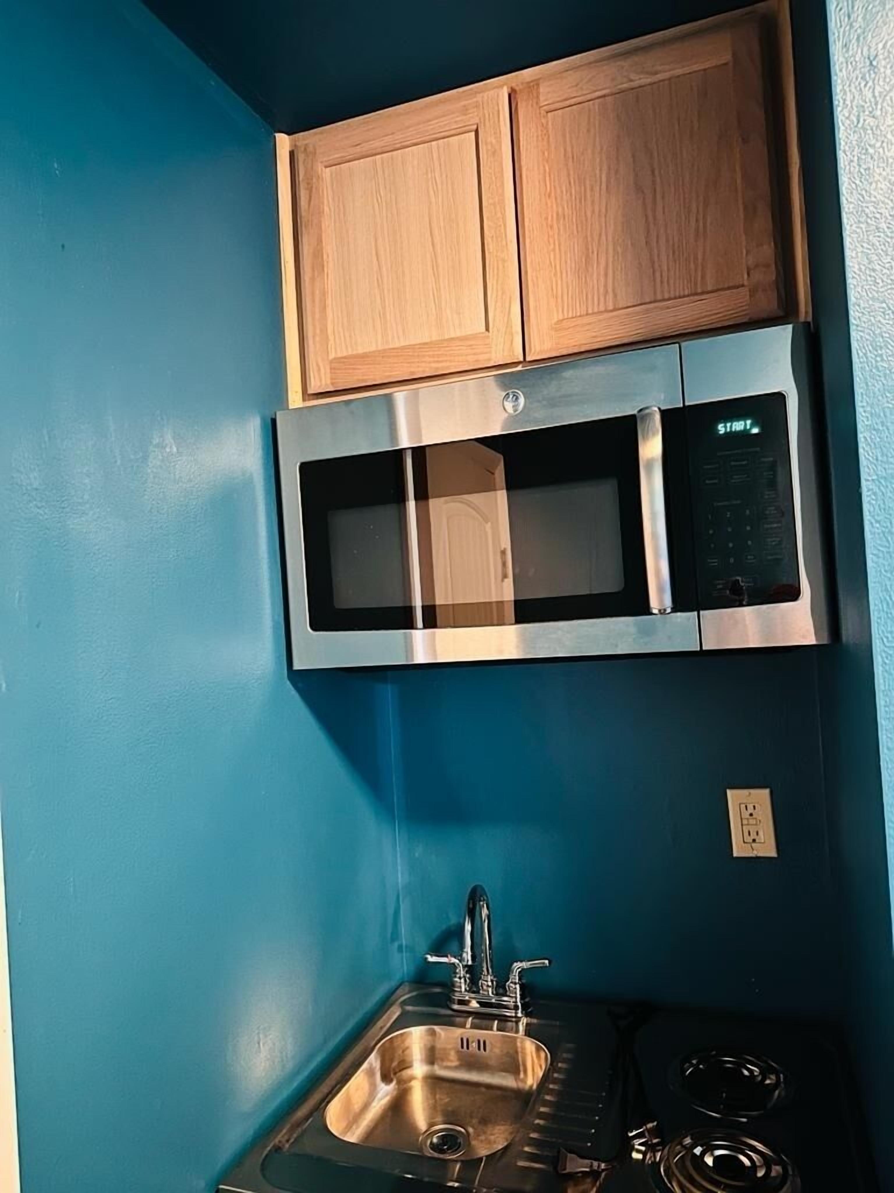 A compact kitchen with a microwave, a sink, and wooden cabinets.