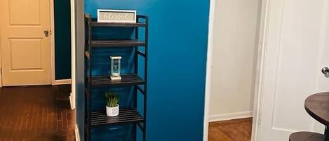 A room with a blue wall, a ceiling fan, a white door, and a shelf with decorative items.