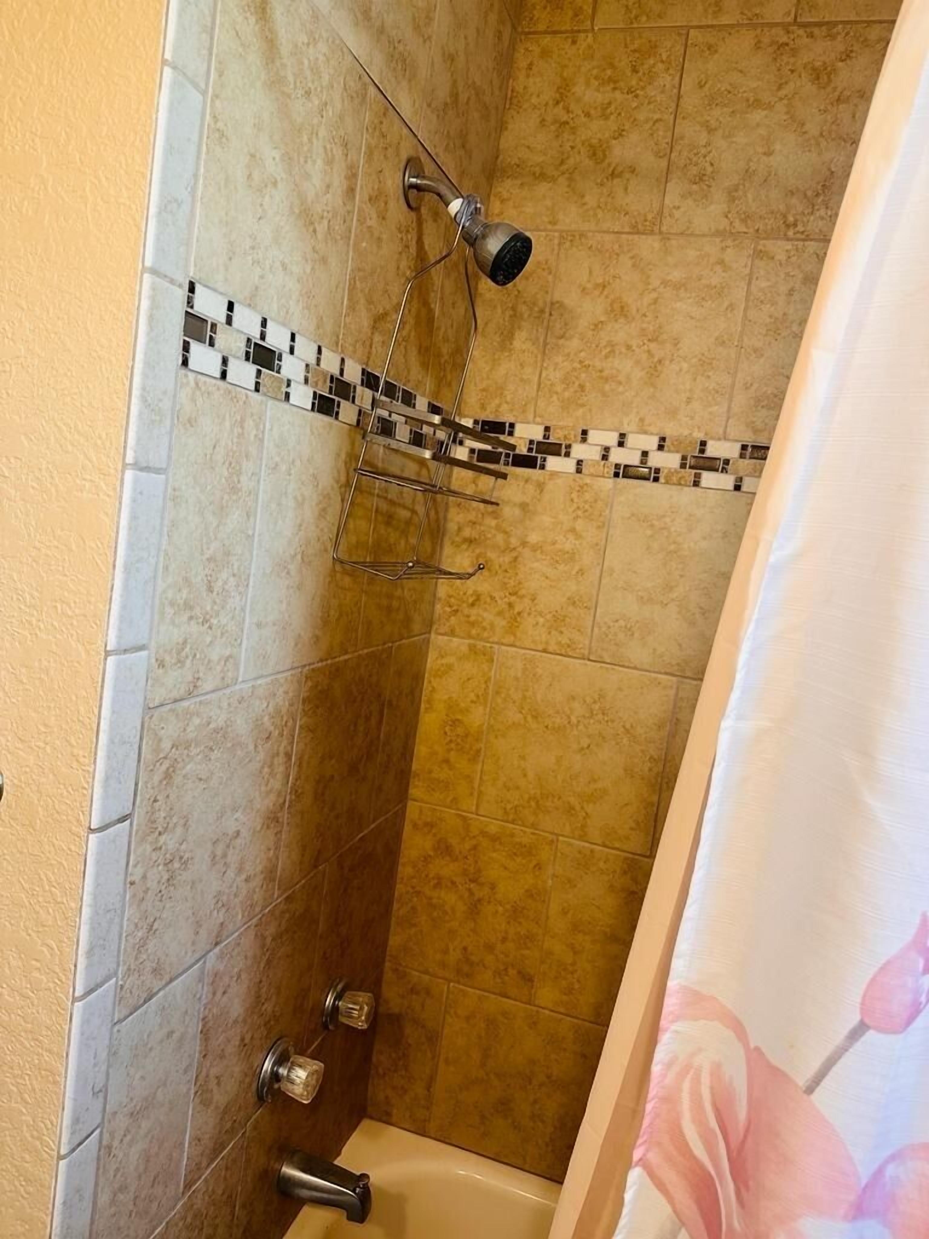 Ein Duschbereich mit gefliesten Wänden, einer Duschbrause und einem Wasserhahn.