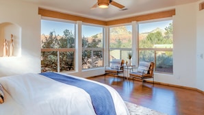 A spacious bedroom with a large bed, a ceiling fan, and multiple windows offering a view of the outdoors. - Red Rock Mtn View & Fire Pit: Central Sedona Home! (Sedona)