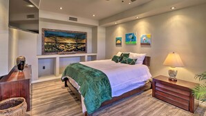 Une chambre à coucher comprenant un lit, une table de chevet, une lampe, un ventilateur de plafond et des œuvres d’art accrochées aux murs.