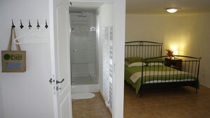 A bedroom with a bed, a shower, and a door with a towel rack.