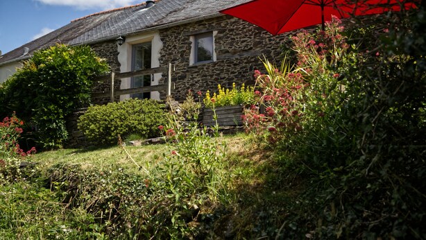 A stone house with a sloped roof and a red umbrella.