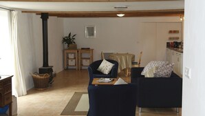 A cozy living room with a fireplace, a dining area with a table and chairs, and a kitchen visible through an open doorway.