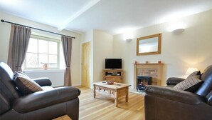 Ein Wohnzimmer mit zwei Ledersofas, einem Holztisch, einem Fernseher auf einem Standfuß und einem Kamin.