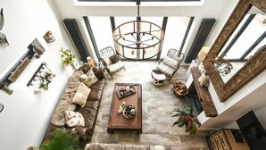 A spacious living room with a high ceiling, a central chandelier, a sectional sofa, and a coffee table. - Marmalade Cottage (Seahouses)