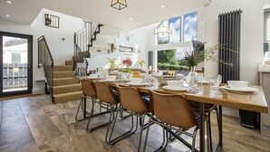 A spacious dining area with a wooden table set for six, surrounded by chairs. A staircase with a metal railing leads to an upper level. - Marmalade Cottage (Seahouses)