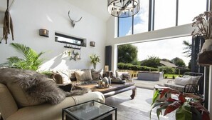 A spacious living room with a large window, a sofa, a coffee table, and a dining area. - Marmalade Cottage (Seahouses)