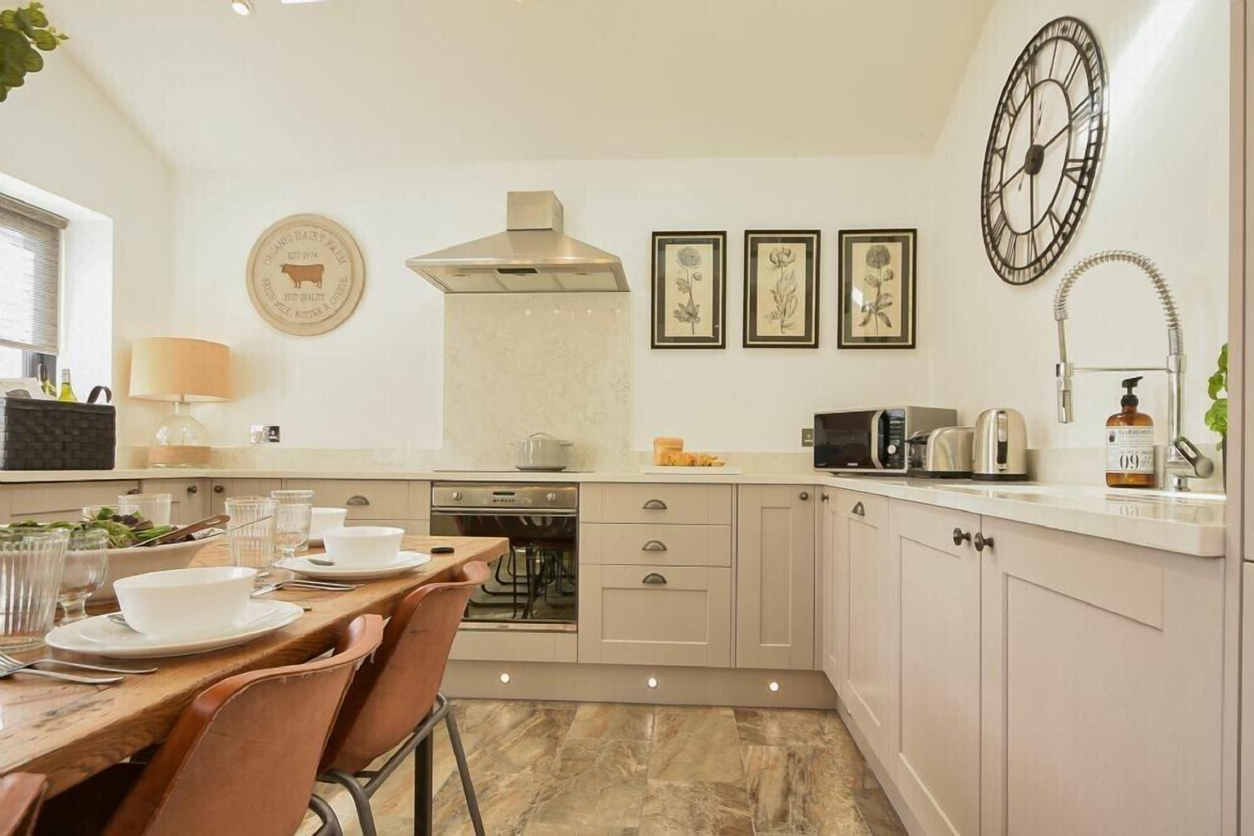 A modern kitchen with a dining area, featuring a stove, oven, microwave, and a clock on the wall.