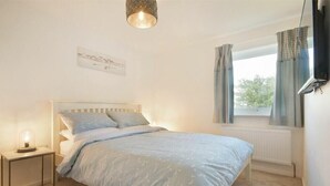 Une chambre à coucher avec un lit, une lampe de chevet, une fenêtre avec des rideaux et un téléviseur fixé au mur.