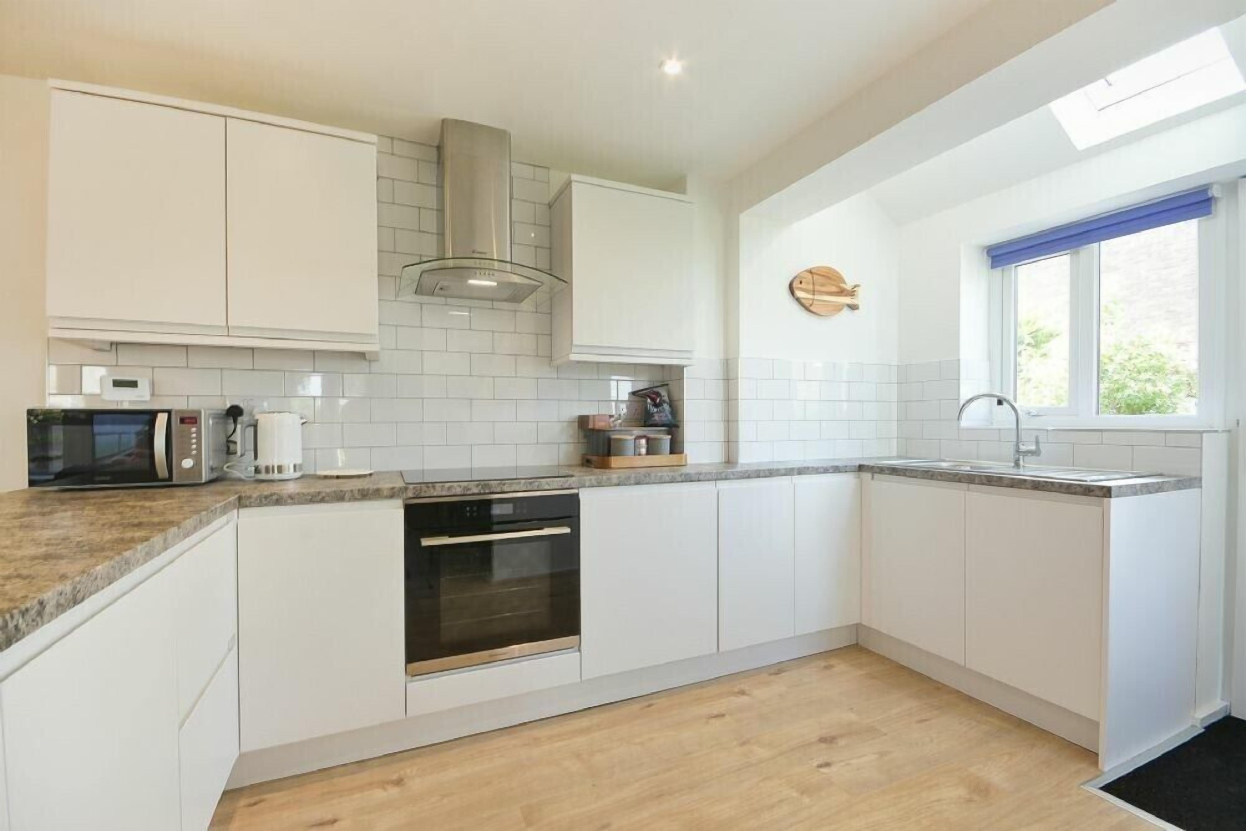 A modern kitchen with white cabinets, a built-in oven, a microwave, and a coffee maker.