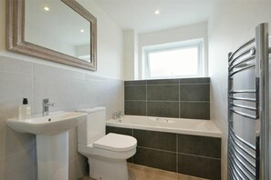 A modern bathroom with a white sink, toilet, and bathtub. - Coastal Plaice (Chathill)