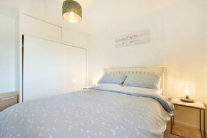 A bedroom with a bed, bedside table, and a hanging light fixture. - Coastal Plaice (Chathill)