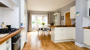 A modern kitchen with wooden flooring, white cabinetry, and a dining area with a table and chairs. - The Beach House, Alnmouth (Alnwick)
