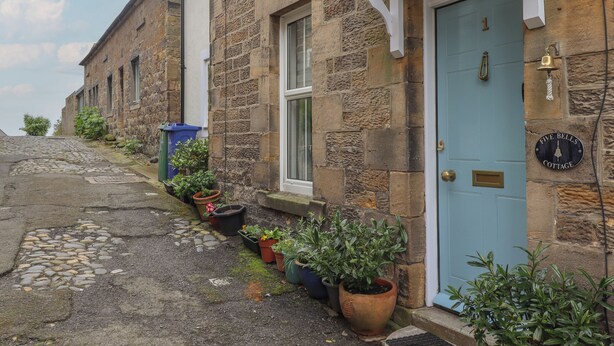 A stone building with a blue door, potted plants, and a 'Five Bells Cottage' sign. - Five Bells Cottage (Alnwick)