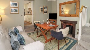A living room with a sofa, chairs, a dining table, a fireplace, and a TV. - Five Bells Cottage (Alnwick)