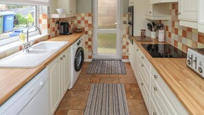 A compact kitchen with a washing machine, sink, and stove. - Five Bells Cottage (Alnwick)