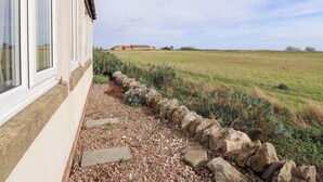 A house with a stone wall and a gravel path leading to a grassy field. - Beach View (Seahouses)