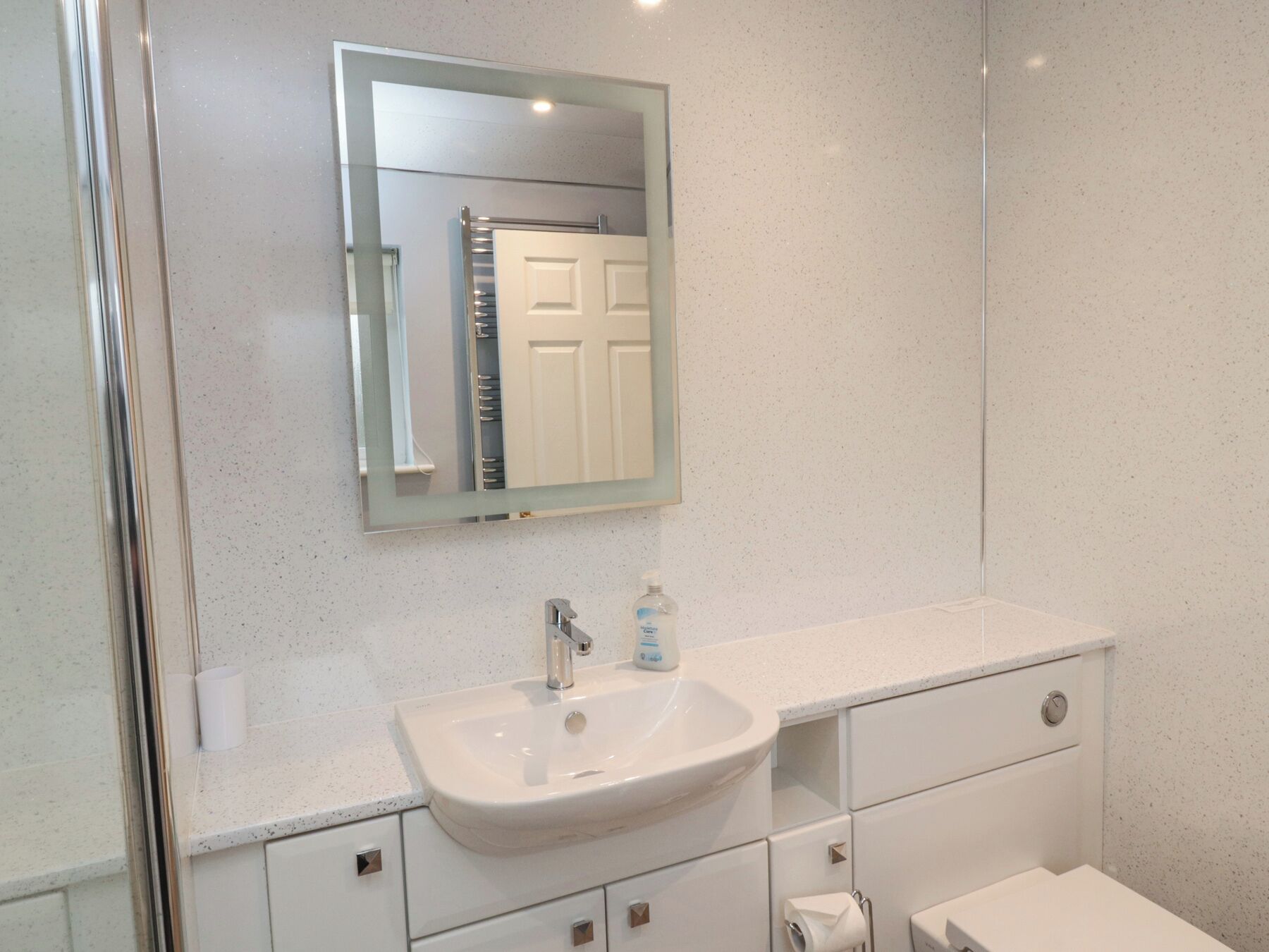 Une salle de bain moderne avec un lavabo blanc, un miroir et une porte en arrière-plan.