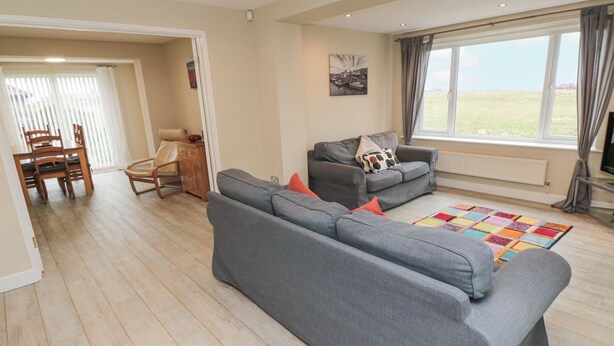 A spacious living room with a grey sofa set, a wooden dining table with chairs, and a colorful rug. - Beach View (Seahouses)