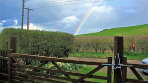 Een landelijk landschap met een regenboog, een houten poort en een veld.