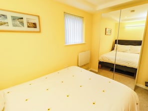 A bedroom with a bed, a window with blinds, a radiator, and a mirror reflecting the bed.