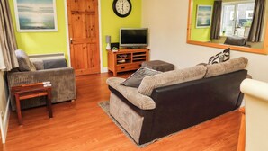 A living room with a sofa, a television, a clock, and a door.