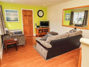 A living room with a sofa, a television, a clock, and a door.