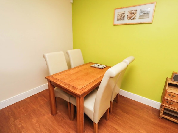 A dining area with a wooden table and four chairs, a small table with a menu, and a framed picture on the wall.