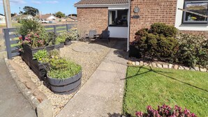 A residential property with a brick exterior, a small garden with raised flower beds, a paved driveway, and a door leading to the entrance.