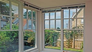 A corner room with large windows overlooking a garden and a residential area. - Stone Cottage (Bamburgh)