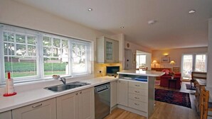 A modern kitchen with white cabinets, a dishwasher, and a dining area with a red sofa and a small table. - Stone Cottage (Bamburgh)