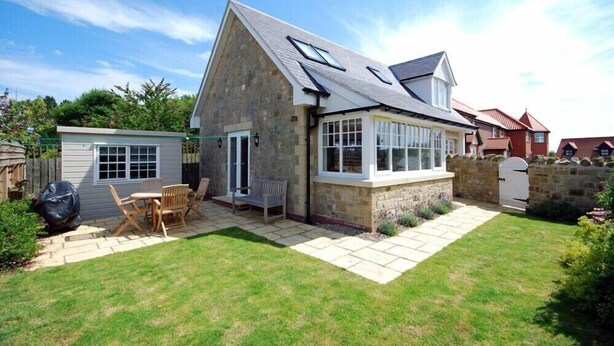 A house with a stone exterior, a sloped roof, and a patio with outdoor furniture. - Stone Cottage (Bamburgh)