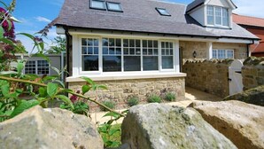 A house with a stone facade, a pitched roof, and a large windowed front. - Stone Cottage (Bamburgh)
