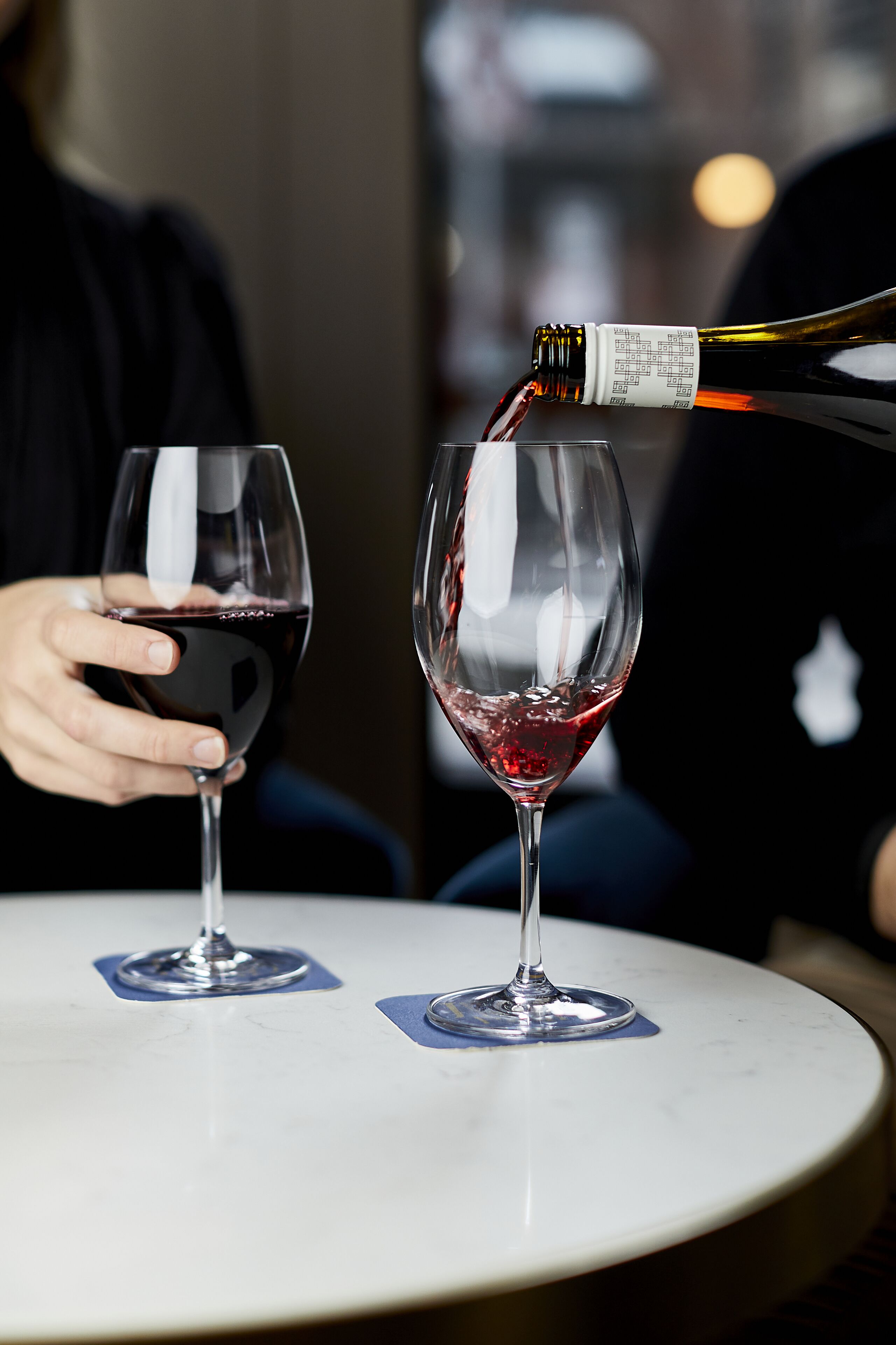 Two wine glasses on a round table with a bottle being poured into one of them.