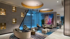 Un moderno vestíbulo de hotel con una zona de estar curva, un ventanal grande y una pared abstracta de colores.