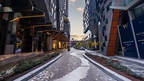 Una calle urbana moderna con un camino pavimentado, edificios a ambos lados y un cartel anunciando apartamentos a la venta.