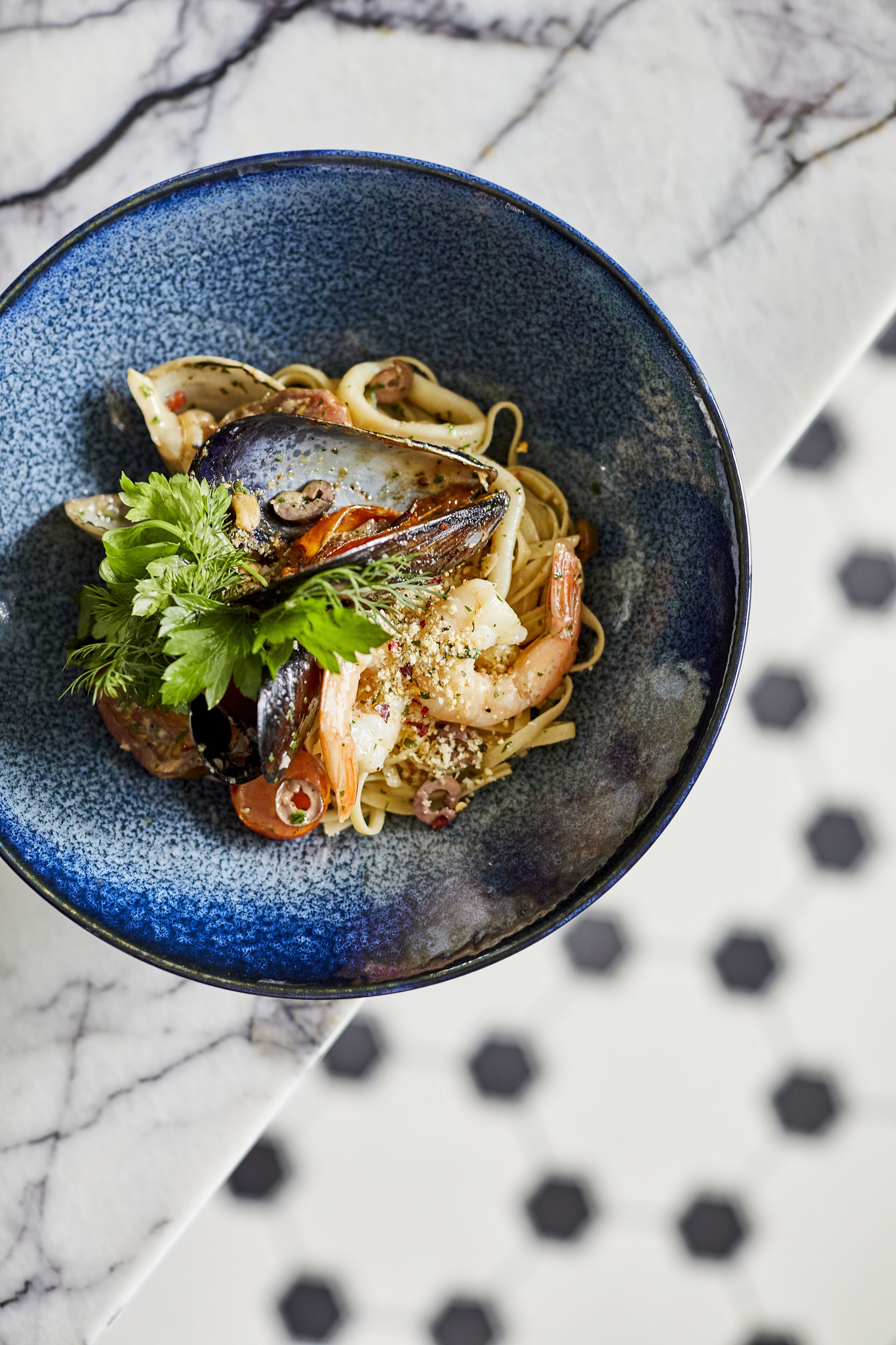 Un plato azul con pasta, mariscos y hierbas.