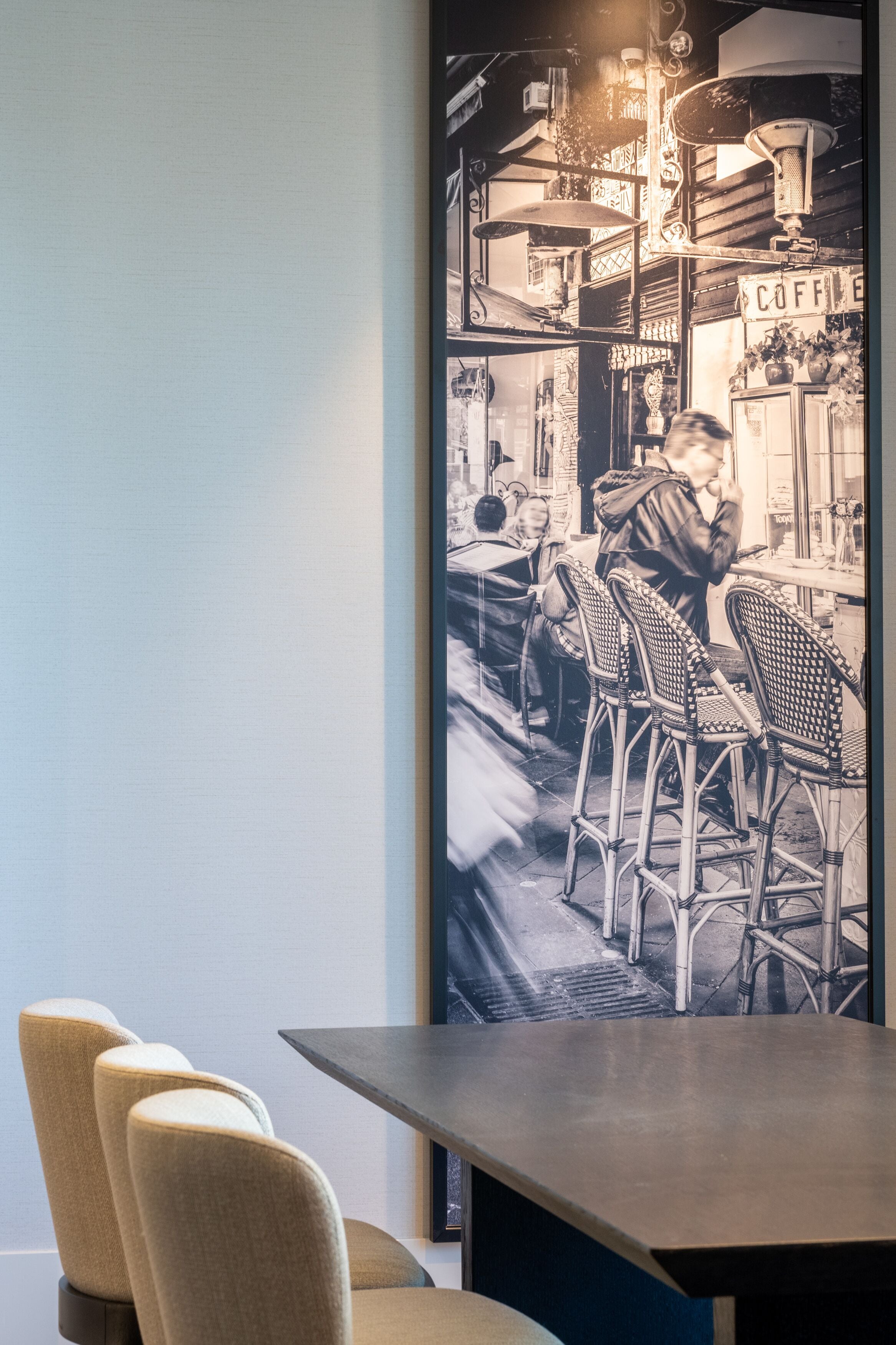 L’intérieur d’un café, avec des chaises en osier, une table et une enseigne ancienne sur laquelle on peut lire « CAFÉ ».