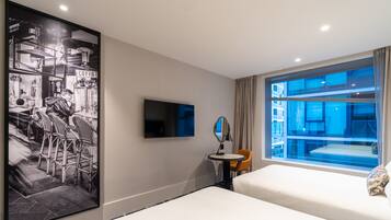 A hotel room with a bed, a TV, a small table with a chair, a large window, and a wall-mounted mirror.