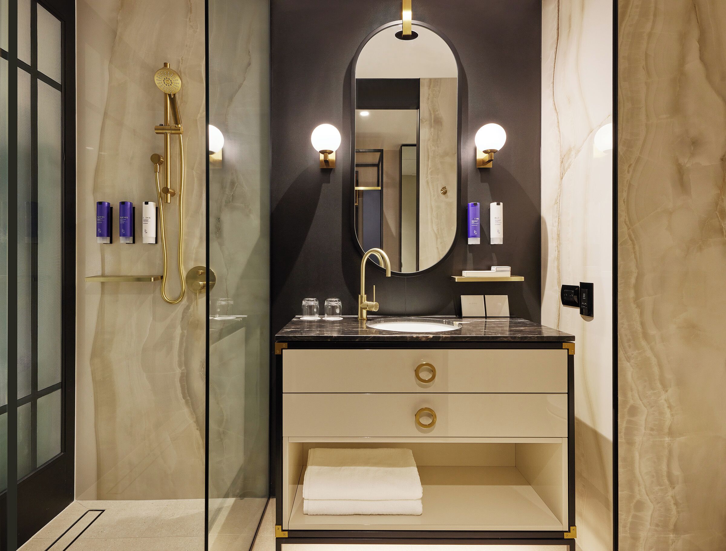 A modern bathroom with a marble vanity, a gold showerhead, and a large mirror.