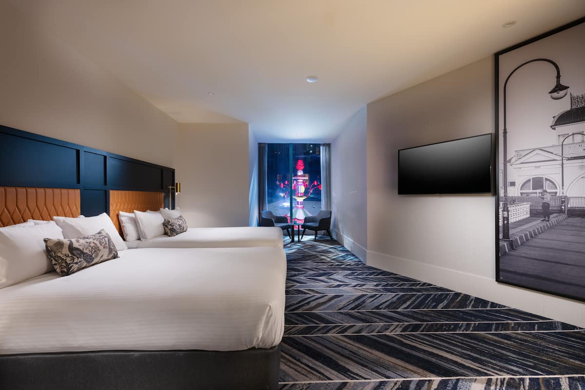 A hotel room with two beds, a flat-screen TV mounted on the wall, and a patterned carpet.