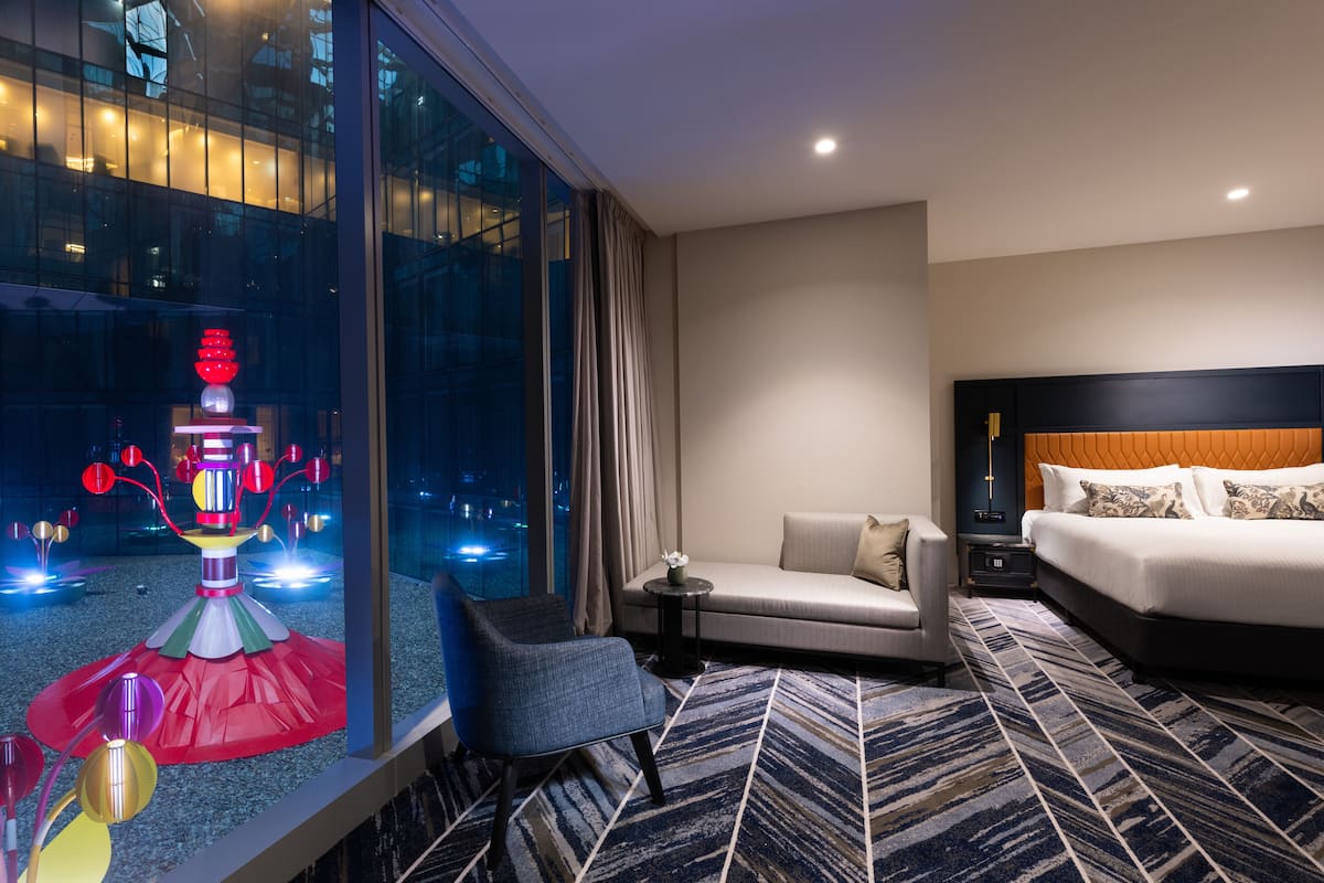 A modern hotel room with a large window, a sofa, a bed, and a small table.