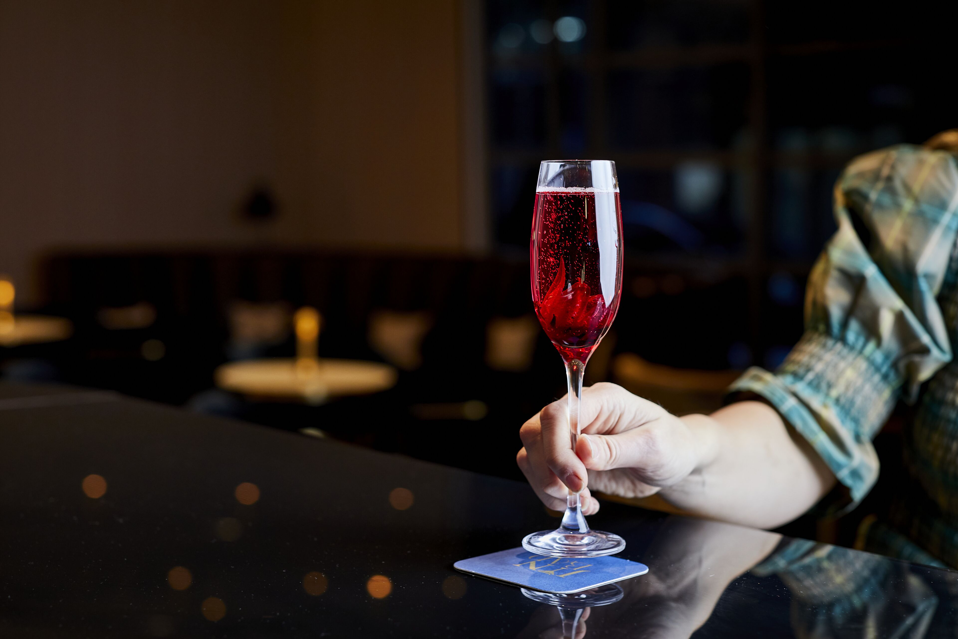 A hand holding a wine glass on a table with a card underneath.