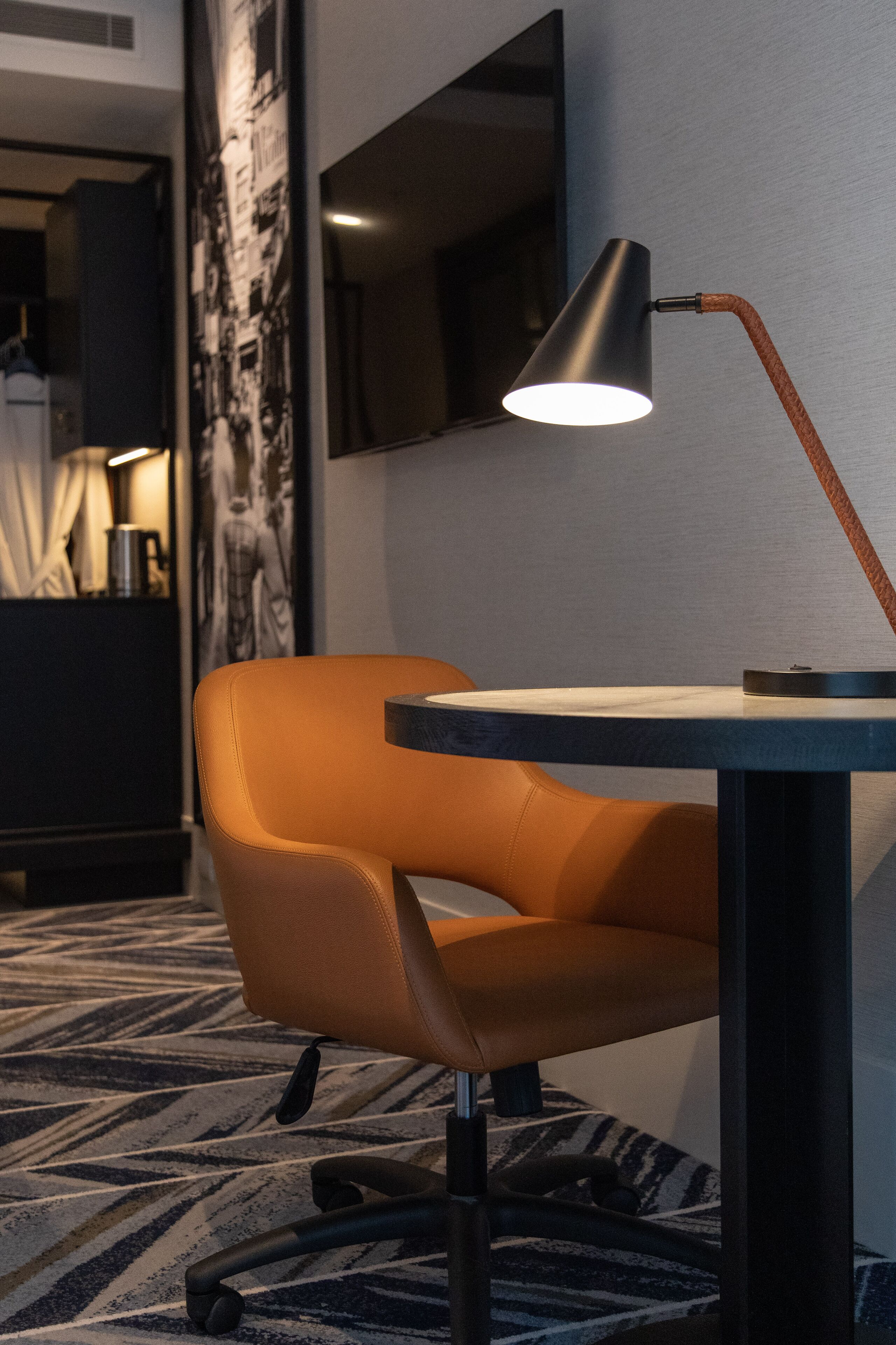 A modern hotel room with a leather chair, a table, a lamp, and a large wall art piece.