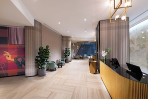 A modern hotel lobby with a reception desk, seating area, and decorative plants.
